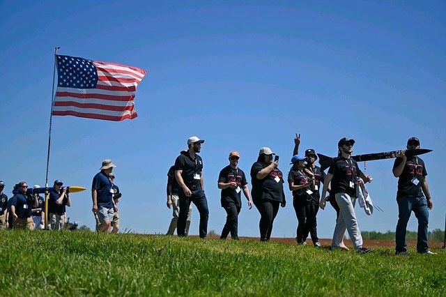 LUNAR team members walking across a launch field beneath an American flag.
